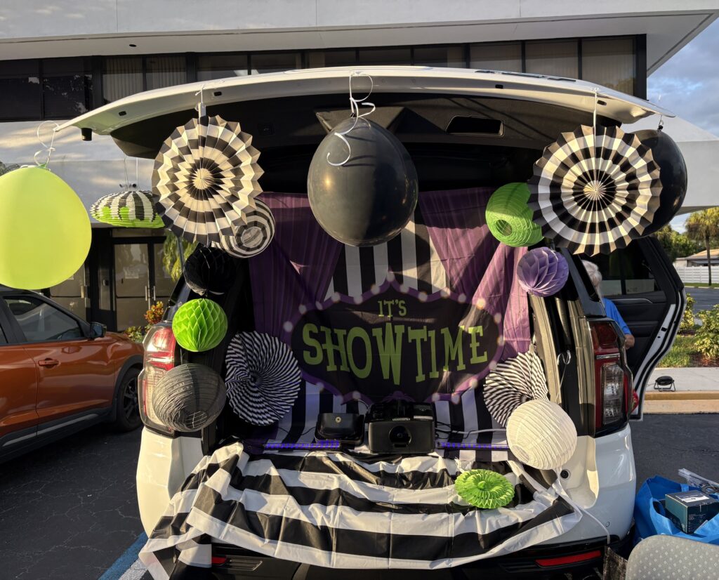 An open SUV trunk decorated with black-and-white striped paper fans, black and green balloons, purple curtains and an It's Showtime marquee sign.